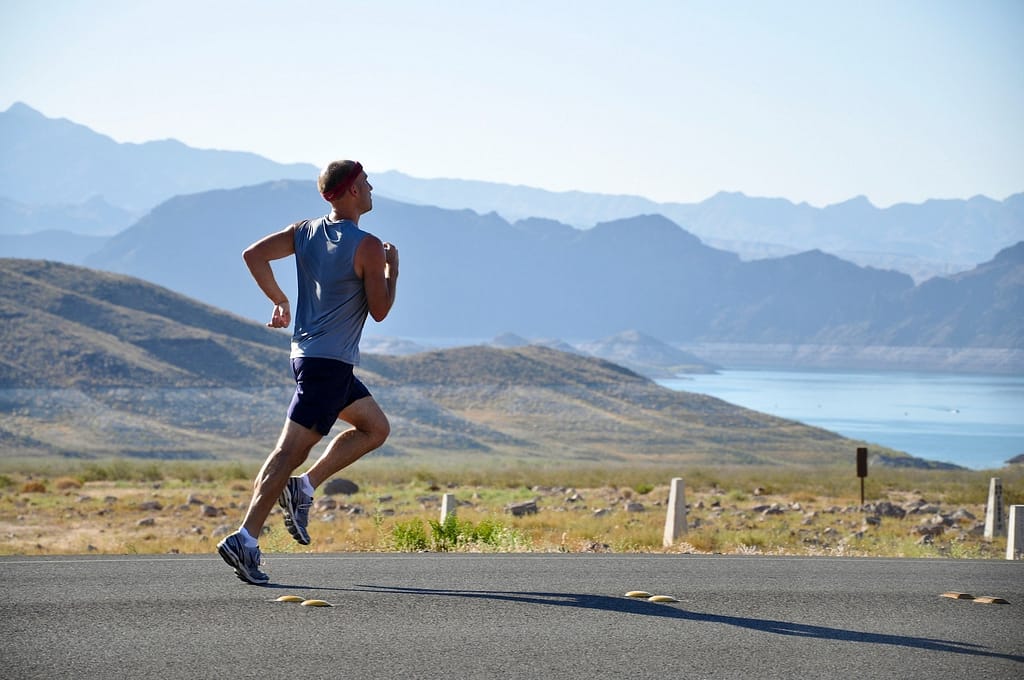 An individual running near majestic mountains and a serene lake, enjoying outdoor exercise and nature.