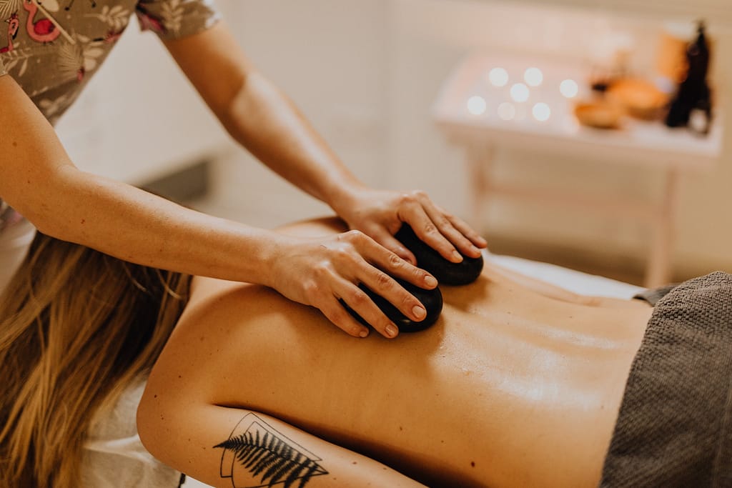 Hands placing heated stones on a client's back during a hot stone massage session for relaxation and muscle tension relief.